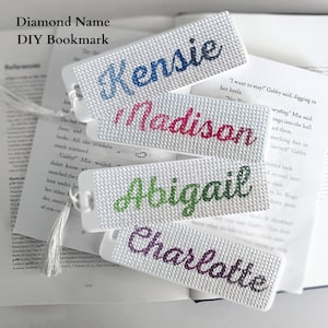 May include: Four white bookmarks with different names written in colorful rhinestones. The names are Kensie, Madison, Abigail, and Charlotte. The bookmarks are on top of a book.