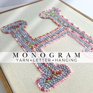 May include: A punch needle letter H monogram on off-white fabric, framed in wood. The letter features a textured, multi-colored yarn design in shades of pink, light blue, and green. The text MONOGRAM YARN LETTER HANGING is centered on the image.
