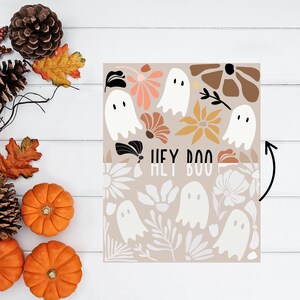 May include: A beige Halloween-themed print featuring white ghost illustrations and floral designs. The text "HEY BOO" is displayed in a brown font. The image is surrounded by pumpkins, pinecones, and autumn leaves.