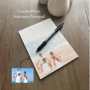 May include: A custom photo stationary notepad featuring a printed illustration of a family of four on a beach, with the names Michael, Liz, Hudson, and Ally at the top. A black retractable ballpoint pen rests diagonally across the notepad surface.