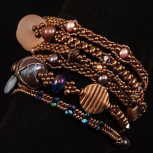 Puede incluir: Un brazalete de múltiples hilos con cuentas de cobre, cuentas de vidrio iridiscente y un dije de disco de cobre. El brazalete está hecho con una variedad de diferentes tamaños y formas de cuentas.