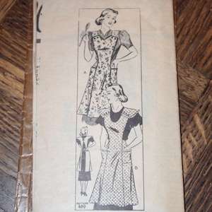 May include: A vintage sewing pattern envelope labeled Pattern 489, featuring black and white line illustrations of two apron styles. Style A shows a floral print apron with pockets, and Style B displays a checkered apron with pockets and shoulder details.
