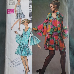 May include: A Simplicity 8729 sewing pattern envelope featuring illustrations of two dress variations. One dress is light blue with a white floral print and bell sleeves, while the other features a vibrant multi-colored floral pattern.
