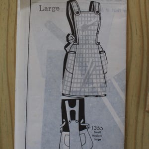 May include: A sewing pattern envelope labeled 1355 Large featuring a line drawing of a gingham apron with shoulder straps and side pockets. The back view shows the strap configuration and the text 1355 Small Medium Large and SUGGESTED FABRICS.