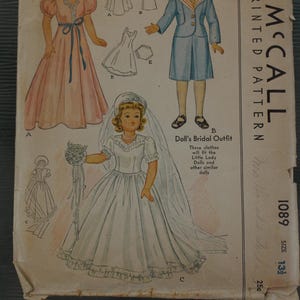 May include: A vintage McCall printed pattern envelope for doll clothing, numbered 1089, size 13 1/2. The front features illustrations of three dolls wearing a pink gown, a blue suit, and a white bridal outfit with a veil, plus line drawings.