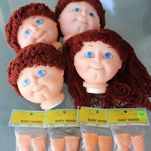 May include: A collection of doll parts, including four doll heads with brown yarn hair and blue eyes, and four packages of baby hands. Each package of baby hands is 2 inches in length.