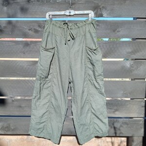 Puede incluir: Pantal&oacute;n de lino verde con cintura de cord&oacute;n y bolsillos grandes. El pantal&oacute;n est&aacute; colgado en una percha contra un fondo de madera.