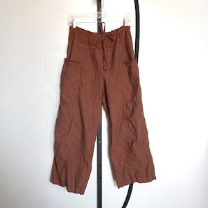 Puede incluir: Pantal&oacute;n de lino marr&oacute;n con cintura de cord&oacute;n y bolsillos grandes. El pantal&oacute;n tiene un corte holgado y una pierna ancha.