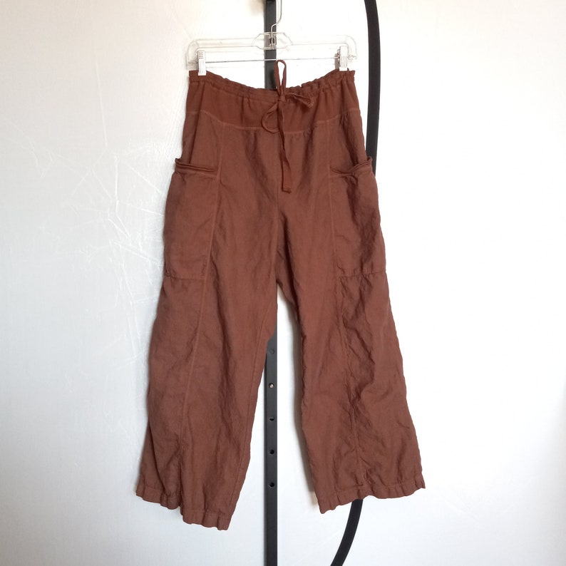 Puede incluir: Pantal&oacute;n de lino marr&oacute;n con cintura de cord&oacute;n y bolsillos grandes. El pantal&oacute;n tiene un corte holgado y una pierna ancha.