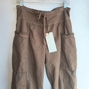 May include: Brown linen trousers with a drawstring waist and two large pockets on the front. The trousers have a relaxed fit and are made of a lightweight fabric. The tag on the trousers reads "odd numbers".