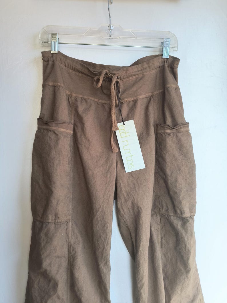 May include: Brown linen trousers with a drawstring waist and two large pockets on the front. The trousers have a relaxed fit and are made of a lightweight fabric. The tag on the trousers reads "odd numbers".