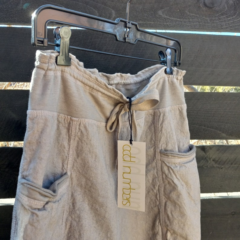 May include: A light beige linen skirt with a drawstring waist and two large pockets. The skirt has a tag that says "Sea & Numbers".