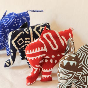May include: Four fabric elephant plushies in different colors and patterns. The elephants are blue, black and white, red and white, and brown and white.