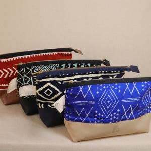 May include: Four different patterned zippered pouches. The pouches are stacked on top of each other. The top pouch is red with a black and white geometric pattern. The second pouch is navy blue with a white and blue geometric pattern. The third pouch is black with a white and blue geometric pattern. The bottom pouch is blue with a white geometric pattern and a tan bottom.