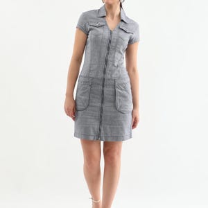 May include: A gray denim dress with a zipper down the front and two pockets on the sides. The dress has short sleeves and a collared neckline.