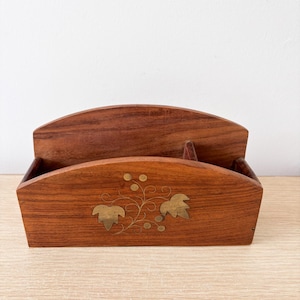 May include: A wooden desk organizer with a curved top and a decorative brass leaf and vine design. The organizer is made of a rich, dark brown wood and has a slot for holding items.