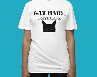 Pode incluir: Camiseta branca com texto preto que diz "Cat Hair, Don't Care." Abaixo do texto, há uma silhueta de gato preto com olhos grandes.