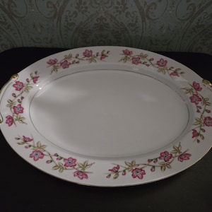 May include: White oval serving platter with a gold rim and pink floral design. The platter has two gold handles.