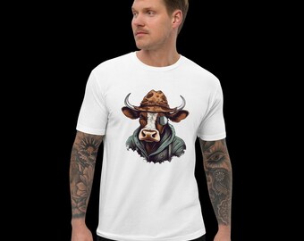 May include: A white short-sleeved t-shirt featuring a graphic print of a brown and white cow wearing a brown hat and a dark green hooded jacket. The cow has a monocle over one eye and prominent horns, centered on the chest of the garment.