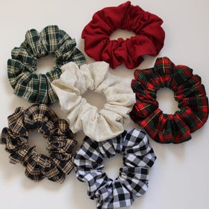 May include: Six fabric scrunchies in various plaid patterns. The scrunchies are in black and white, red and green, green and white, brown and black, and a solid red.