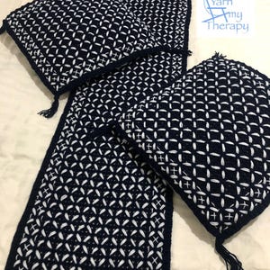 May include: Three crocheted throw pillows and a crocheted runner in a navy blue and white geometric pattern. The pillows and runner have tassels. The text "Yarn My Therapy" is visible in the upper right corner of the image.