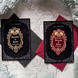 Könnte beinhalten: Zwei Hochzeitskarten im Gothic-Stil mit dem Text "Save the Date". Jede Karte zeigt einen dekorativen Rahmen, Totenköpfe, Rosen und die Namen "Amanda & Jacob" mit dem Datum 05.06.2028. Eine Karte ist goldfarben, die andere rot.