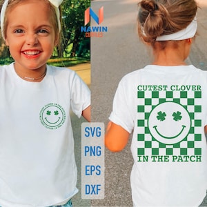 Könnte beinhalten: Weißes T-Shirt mit einem grünen Smiley mit Kleeblättern als Augen und dem Text "Cutest Clover in the Patch" um das Gesicht. Das Shirt wird von einem Kind modelliert.