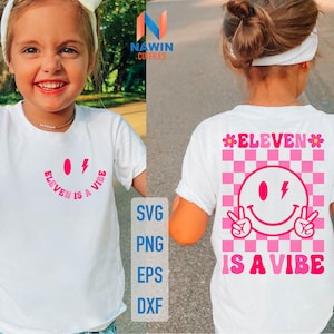 Op de afbeelding: Wit T-shirt met een roze smiley en de tekst "ELEVEN IS A VIBE". De achterkant van het shirt heeft een roze dambordpatroon met een smiley en de tekst "ELEVEN IS A VIBE".