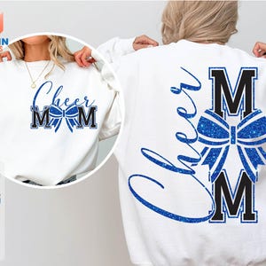 May include: White sweatshirt with the text "Cheer Mom" in blue and black, featuring a bow graphic. The back of the sweatshirt also displays "Cheer" and "M" with a bow graphic. The design is a glittery blue.