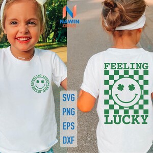 Può includere: Due magliette bianche con un design a trifoglio verde. Una maglietta dice "Feeling Lucky" con un'emoticon sorridente con occhi a trifoglio. L'altra maglietta dice "Feeling Lucky" con uno sfondo a scacchi verde e bianco.