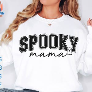 May include: White sweatshirt with the words "SPOOKY mama" in black block letters and a ghost graphic. The sweatshirt also has the words "SVG, PNG, EPS, DXF" in blue letters.