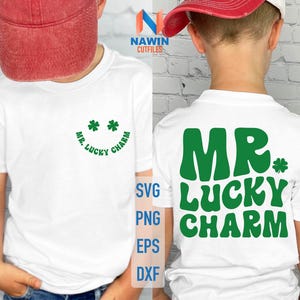 Puede incluir: Camiseta blanca con texto y gráficos verdes. La parte delantera presenta una cara sonriente con tréboles y las palabras "MR. LUCKY CHARM". La parte trasera muestra "MR. LUCKY CHARM" en letras verdes grandes con un trébol.