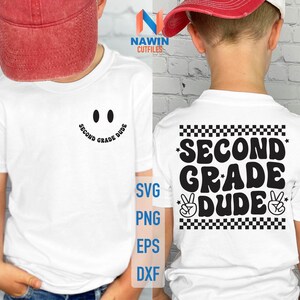 Può includere: T-shirt bianco a maniche corte con la scritta "Second Grade Dude" in nero. La parte anteriore della maglietta presenta un disegno a forma di faccina sorridente. La parte posteriore della maglietta ha un motivo a scacchi e segni di pace.