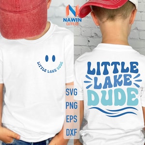 May include: White t-shirt with a blue and white "Little Lake Dude" graphic on the back and a blue smiley face with the same text on the front. The shirt is being modeled by a child wearing a red baseball cap.