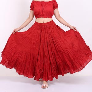 May include: A two-piece red outfit comprising a cropped, off-the-shoulder top and a flowing, tiered skirt. The fabric appears lightweight and textured, creating a bohemian aesthetic. The outfit is designed for a comfortable and stylish look.
