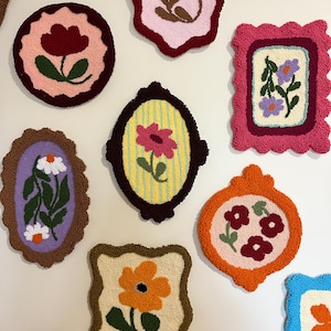 Pode incluir: Uma cole&ccedil;&atilde;o de pe&ccedil;as de arte t&ecirc;xtil floral coloridas e emolduradas. Cada pe&ccedil;a apresenta um design floral diferente em v&aacute;rias cores, incluindo rosa, laranja e roxo, com bordas decorativas. As obras de arte s&atilde;o exibidas em um fundo neutro.