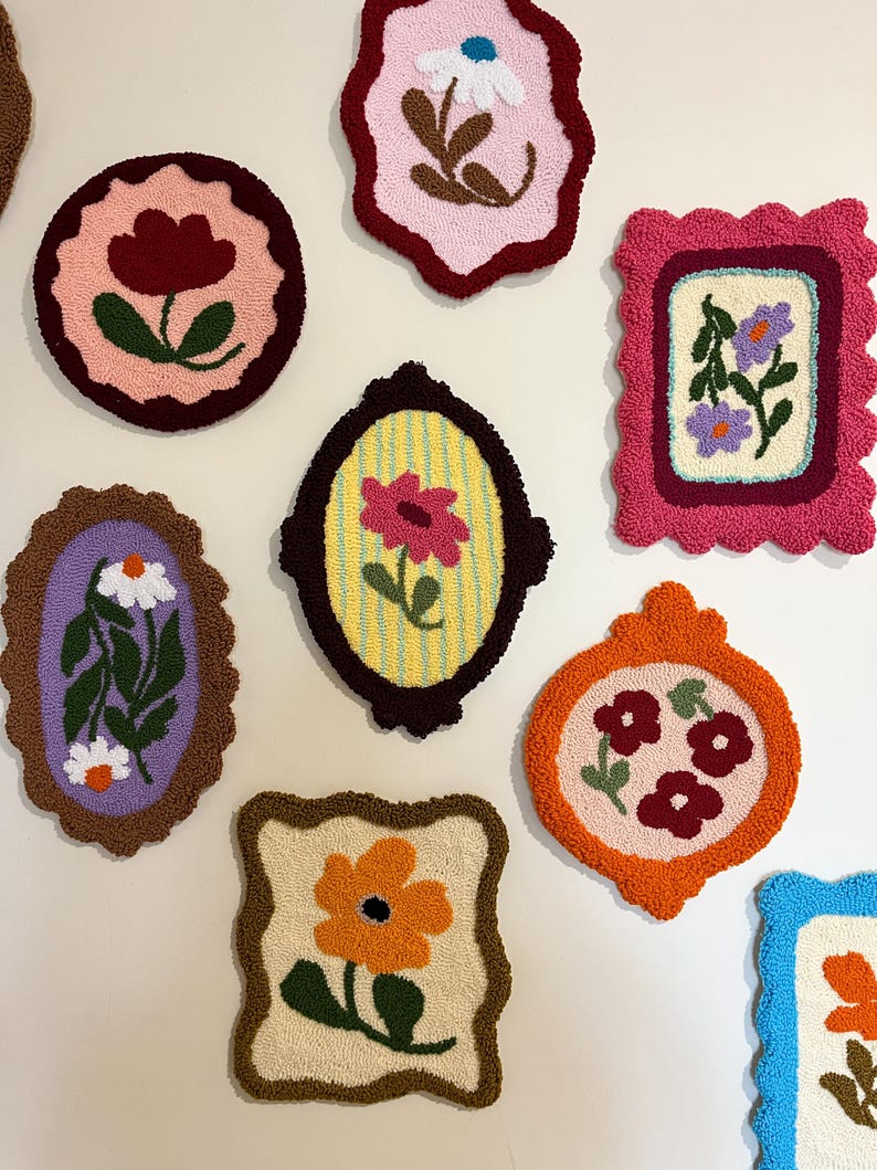 Pode incluir: Uma cole&ccedil;&atilde;o de pe&ccedil;as de arte t&ecirc;xtil floral coloridas e emolduradas. Cada pe&ccedil;a apresenta um design floral diferente em v&aacute;rias cores, incluindo rosa, laranja e roxo, com bordas decorativas. As obras de arte s&atilde;o exibidas em um fundo neutro.