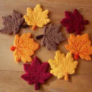 May include: A selection of handmade leaf-shaped decorations in autumnal hues of brown, yellow, orange, and burgundy. The leaves are arranged on a wooden surface, creating a seasonal autumn theme.