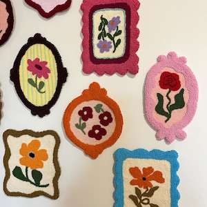 Pode incluir: Uma cole&ccedil;&atilde;o de tape&ccedil;arias de parede florais emolduradas e coloridas. Cada pe&ccedil;a apresenta um design floral diferente, com cores e formas variadas. As molduras t&ecirc;m bordas onduladas e s&atilde;o em tons de rosa, laranja e azul. As flores incluem rosas e margaridas.