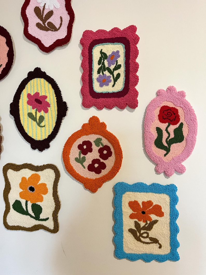 Pode incluir: Uma cole&ccedil;&atilde;o de tape&ccedil;arias de parede florais emolduradas e coloridas. Cada pe&ccedil;a apresenta um design floral diferente, com cores e formas variadas. As molduras t&ecirc;m bordas onduladas e s&atilde;o em tons de rosa, laranja e azul. As flores incluem rosas e margaridas.
