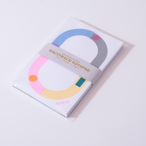 May include: A notepad with a colorful racetrack design. The notepad is wrapped in clear plastic and has a gray band with the text "Racetrack Notepad". The design includes pink, blue, yellow, and orange shapes. The word "NOTES" is printed in pink.
