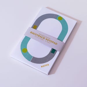 May include: A white notepad with a geometric racetrack design in teal, gray, and yellow. The notepad is held together with a light purple band that reads "Racetrack Notepad". The word "NOTES" is printed in gold.