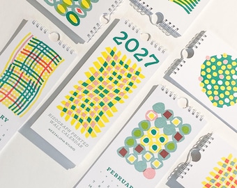 May include: A 2027 risograph printed wall calendar featuring multiple pages with colorful geometric patterns, grid designs, and abstract shapes in shades of green, yellow, pink, and red. Each page includes a monthly calendar grid and spiral binding.