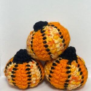 Peut inclure: Trois citrouilles en crochet orange, jaune et noir. Les citrouilles sont empilées les unes sur les autres.