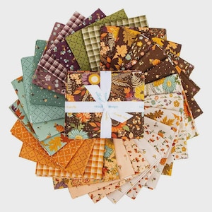 May include: A fabric layer cake bundle featuring a variety of square cotton pieces arranged in a circular fan pattern. The fabrics display autumn-themed prints including leaves, flowers, pumpkins, and plaid patterns in shades of brown, orange, green, and cream. A white ribbon with the text #RileyBlakeDesigns is tied around the center stack.