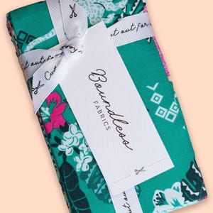 May include: A stack of Boundless Fabrics, wrapped with a white ribbon and tag. The fabric features a teal background with floral and geometric patterns in pink, white, and green. The tag reads "Boundless Fabrics".