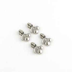 May include: Four silver-colored zipper pulls, each designed with a cherry motif. The cherries have two round spheres and a leaf, adding a decorative touch. These pulls are ideal for adding a unique flair to clothing or accessories.