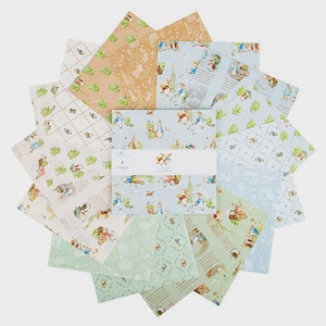 May include: A collection of patterned paper sheets featuring various designs, including illustrations of rabbits and other woodland creatures. The color palette includes light blue, green, and tan hues. The central stack of paper has a white band with the text "Peter Rabbit".