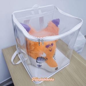 May include: A clear plastic storage bag with a zipper closure, containing a furry orange and white animal head with purple accents. The bag has white straps and is sitting on a wooden surface.