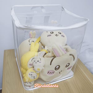 May include: A clear plastic storage bag with a zipper closure, filled with plush toys. The toys are various shades of yellow and cream and feature cartoon faces with brown eyes and pink cheeks.